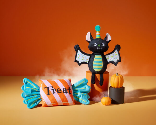 Studio product photography of Halloween-themed pet toys including a bat plush and treat-shaped toy with pumpkins for a commercial pet brand campaign